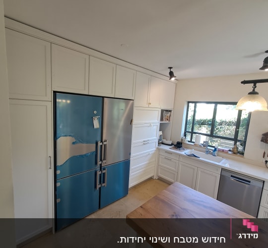 מטבח עם מקרר כחול, ארונות לבנים ושולחן עץ